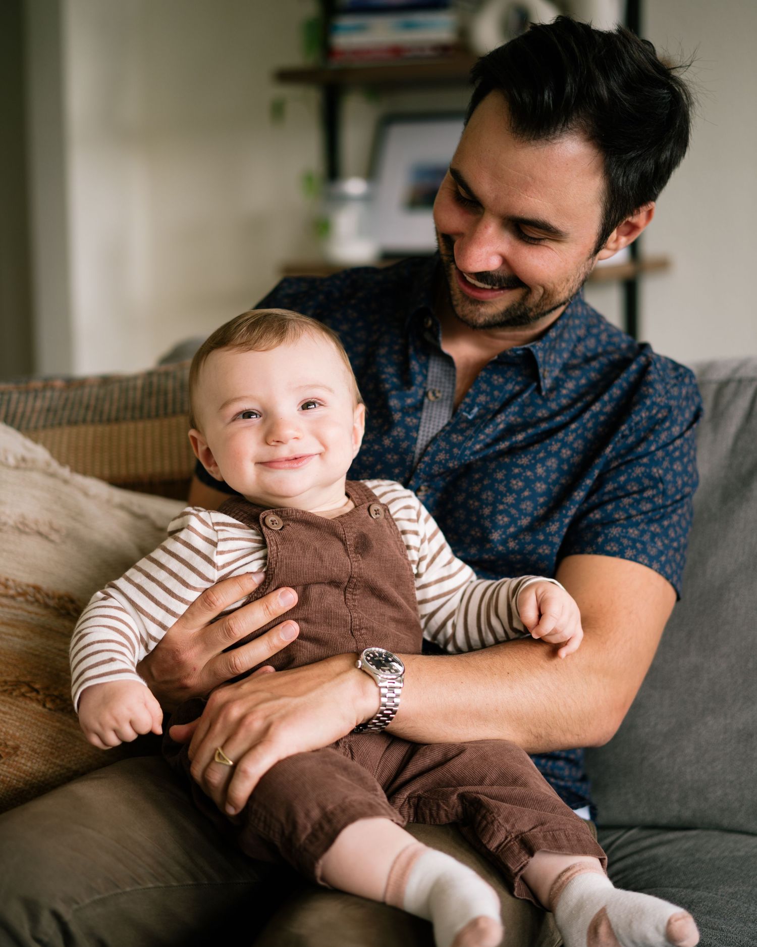 A parent and baby share tender moments on a gray couch while wearing casual clothing.