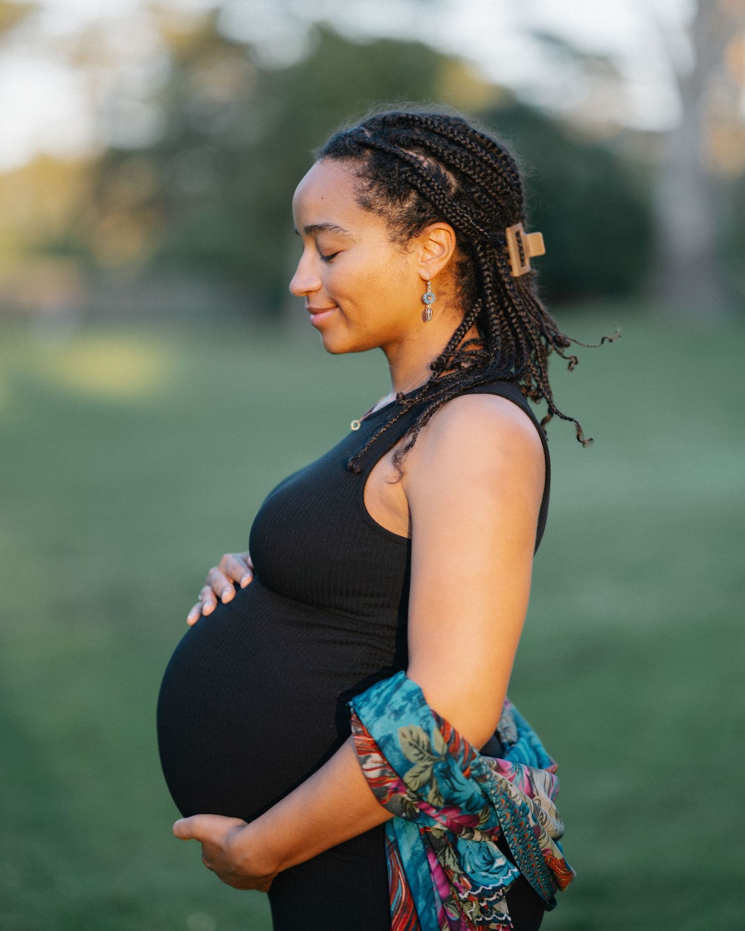 Expectant mother in black dress and colorful shawl poses outdoors during golden hour maternity photoshoot.