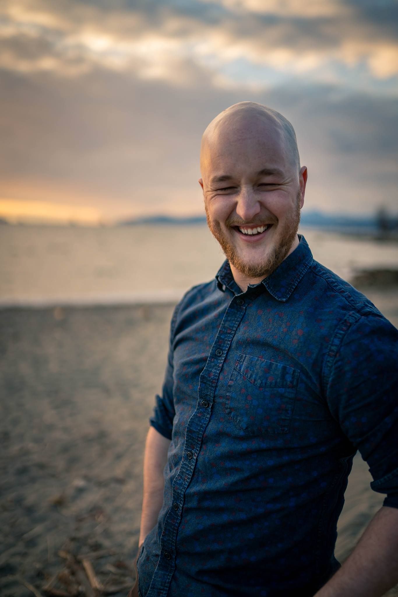A portrait at sunset on a beach with dramatic clouds in the background.