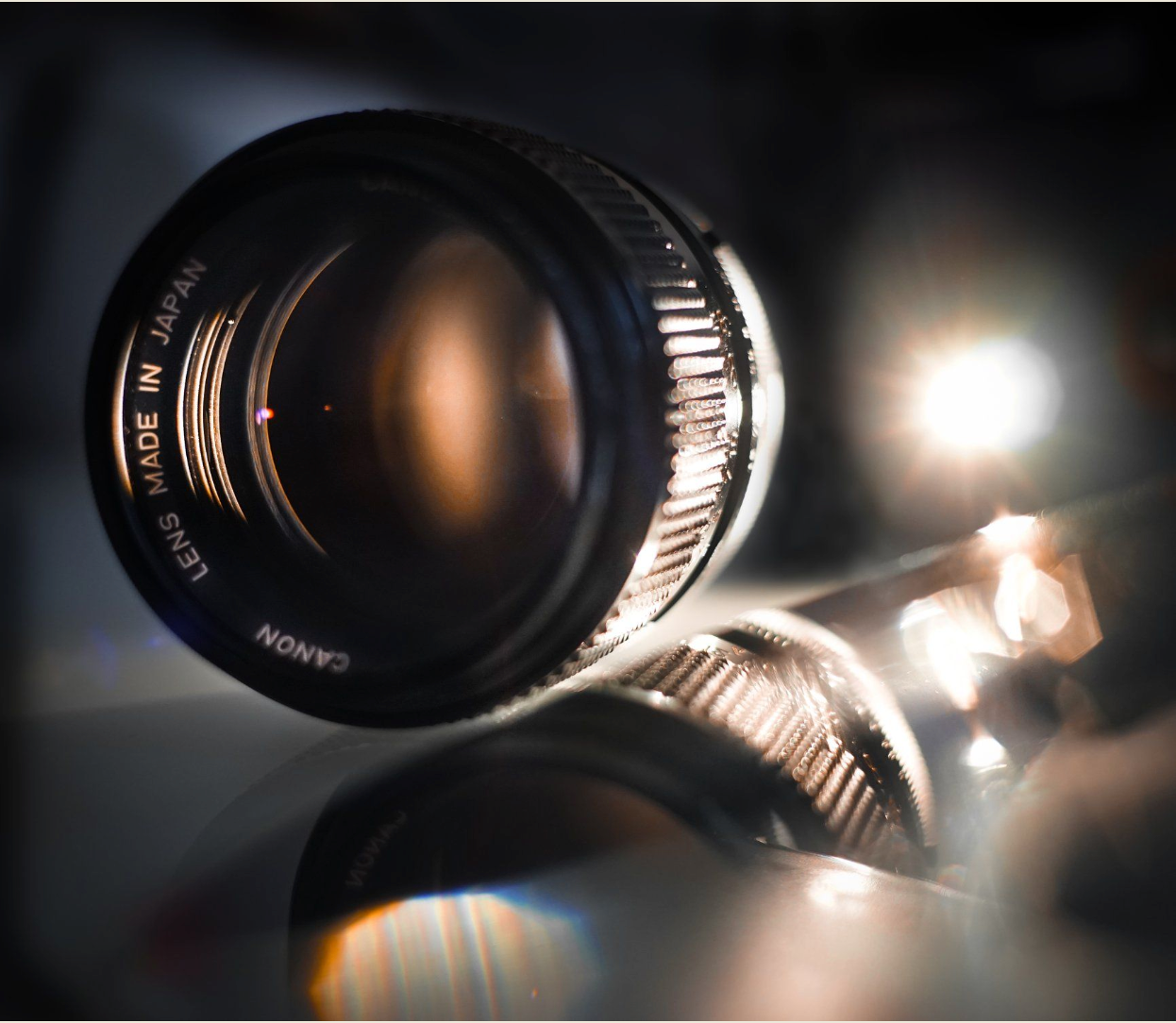 Close-up view of a camera lens with dramatic lighting and reflective surfaces creating artistic bokeh effects.