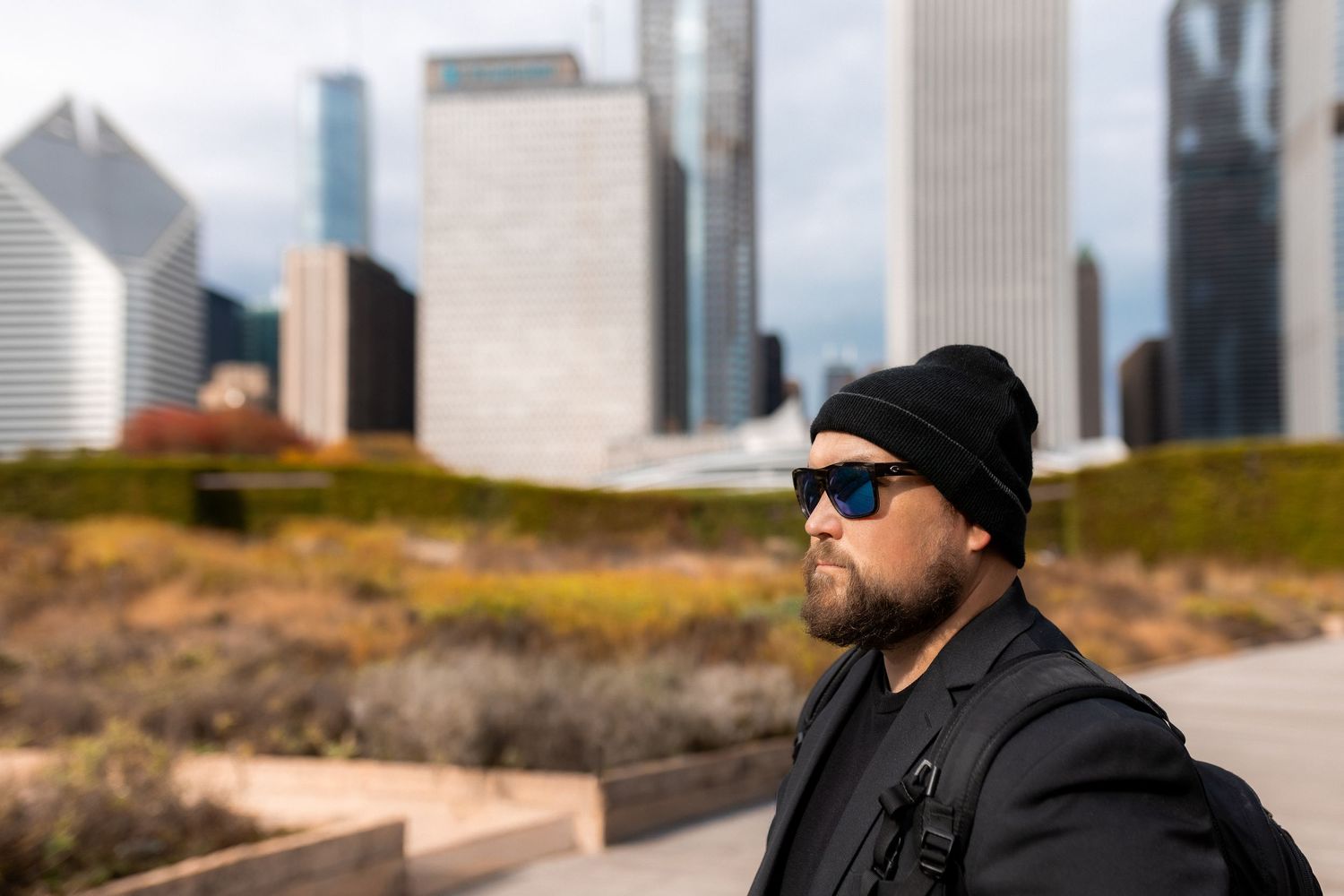 Person in black beanie and sunglasses looks off into distance with city skyline in background.