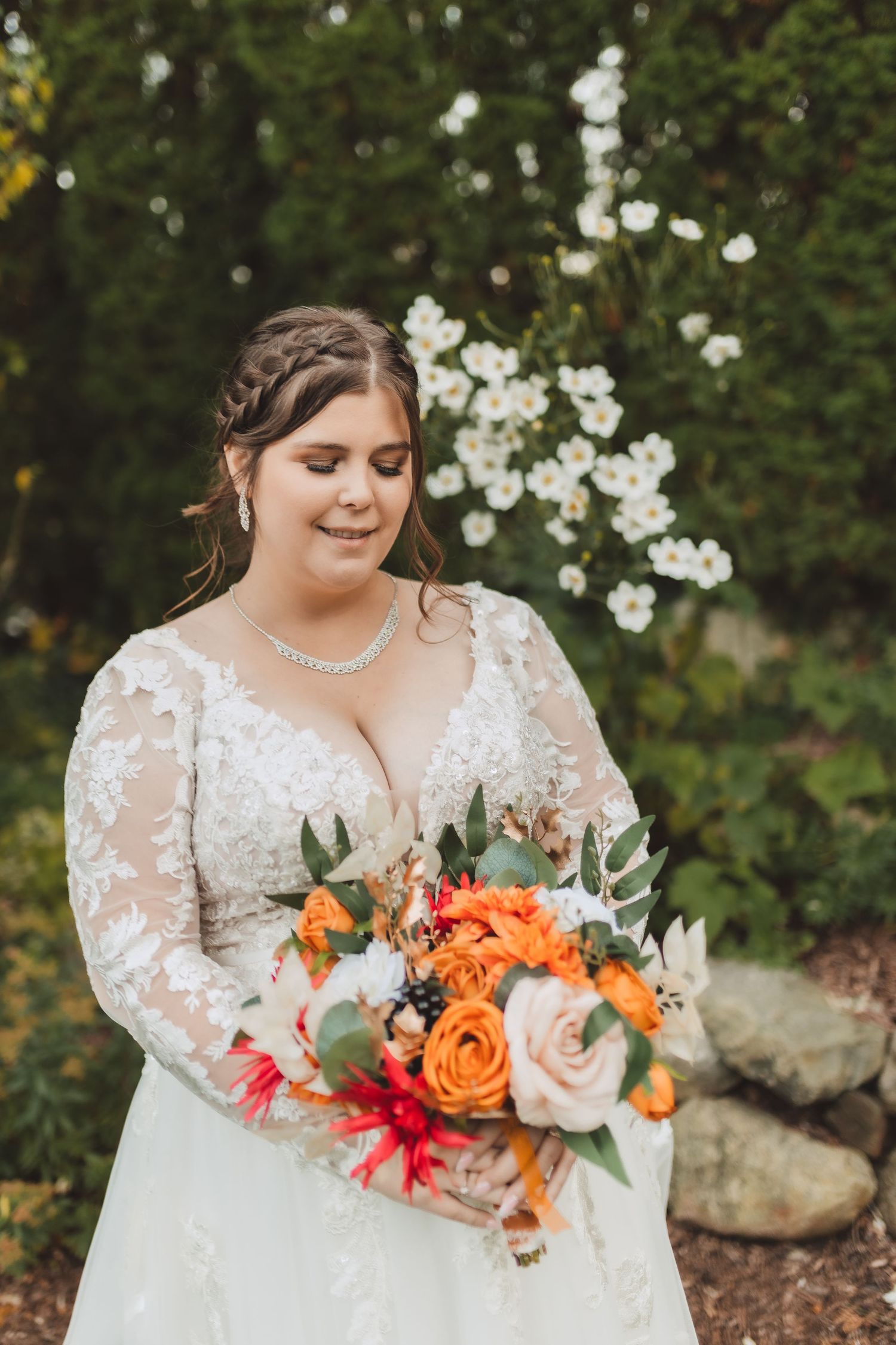 Vibrant orange and red bridal bouquet with roses and greenery against natural outdoor garden background.