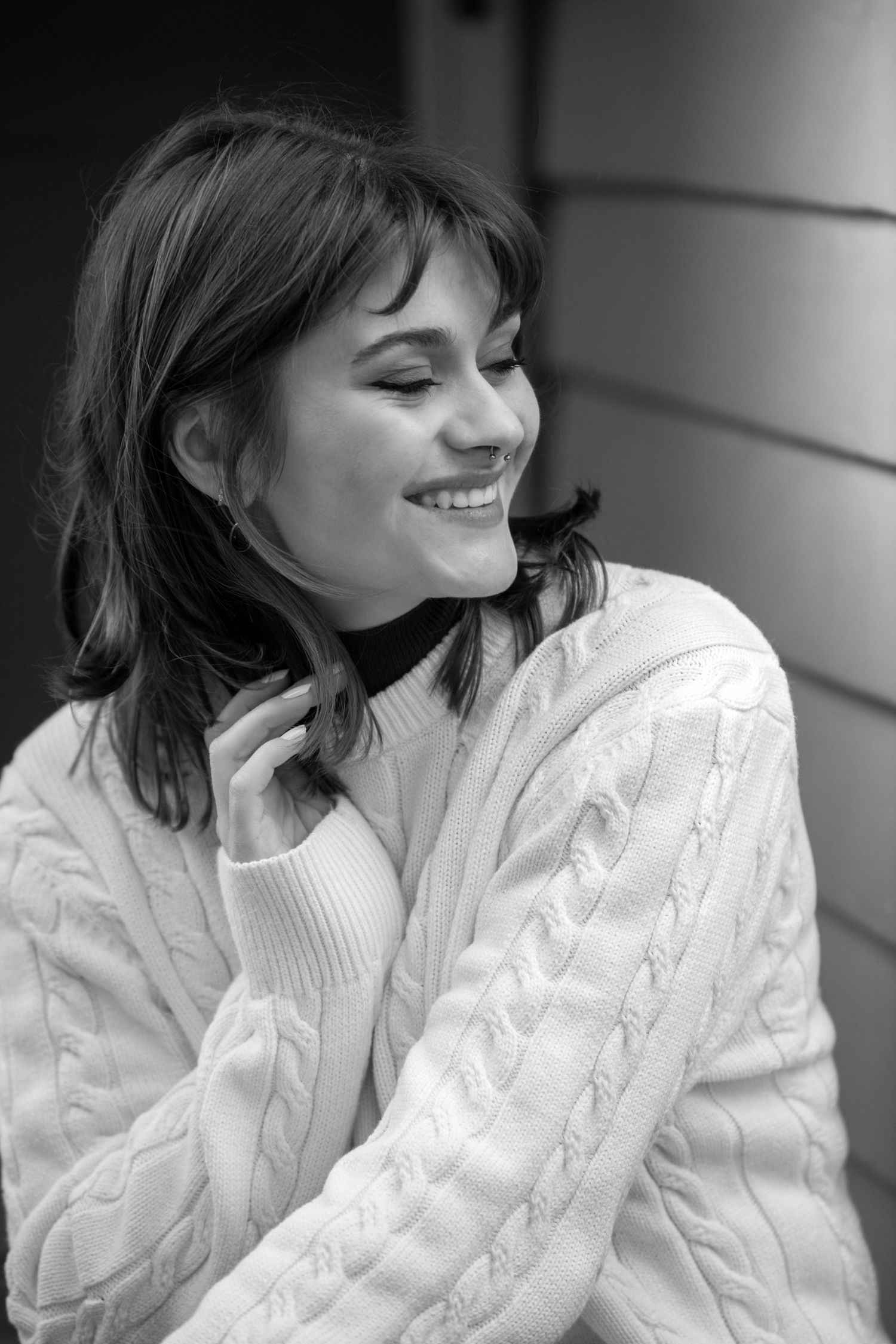 Black and white portrait of someone in a cozy cable knit sweater smiling with eyes closed in a joyful expression.