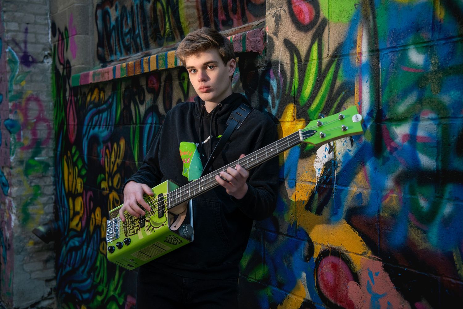 A musician plays an electric guitar against a vibrant graffiti wall with colorful street art in the background.