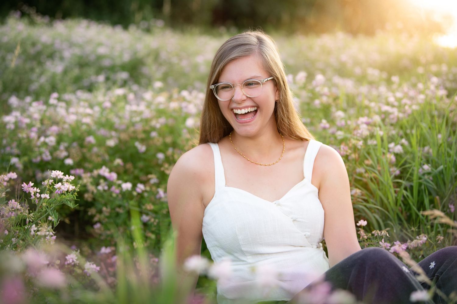 A joyful person in a white top sits in a sunny wildflower meadow filled with pink blooms during golden hour.