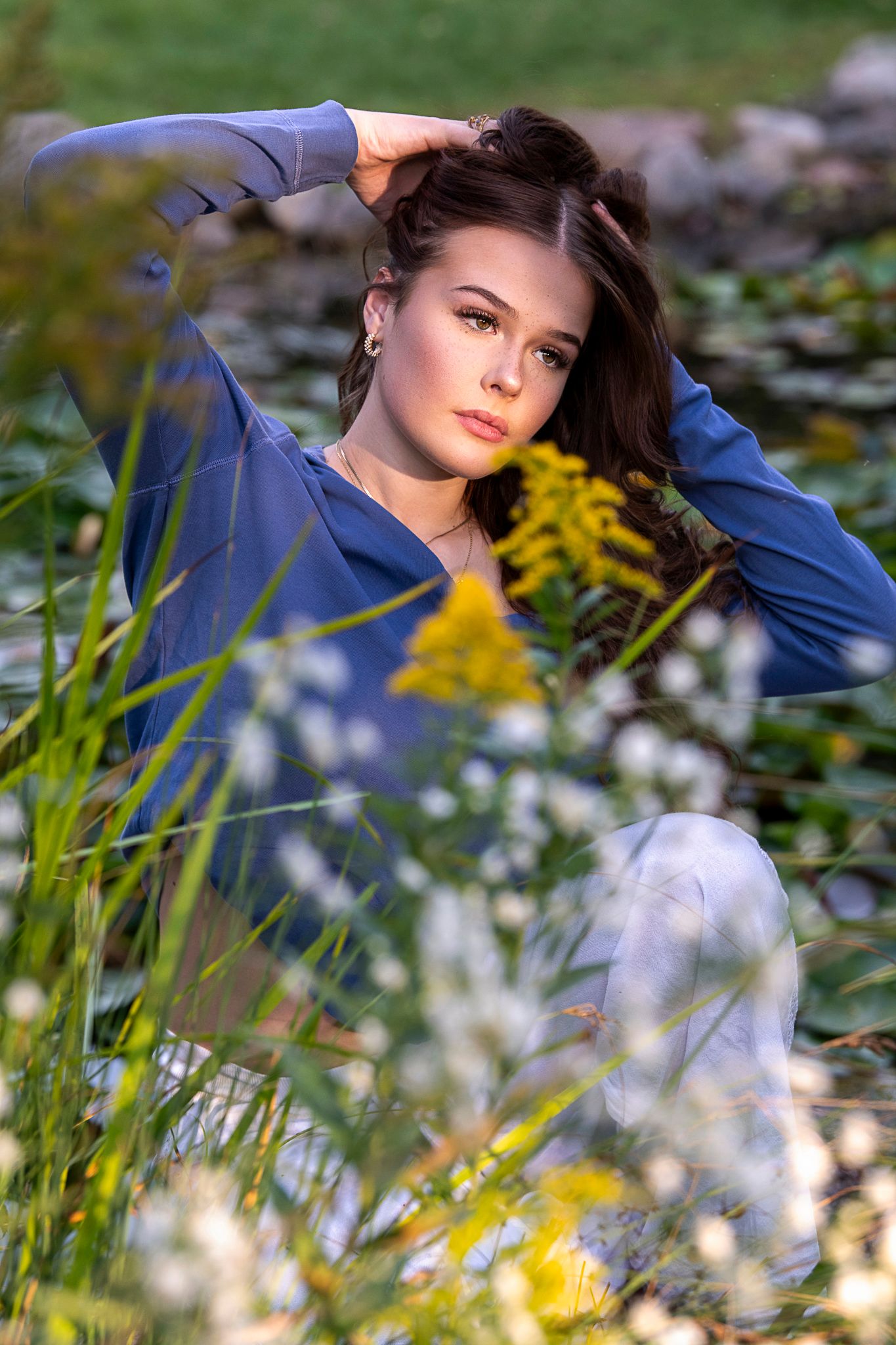Portrait photo taken in a meadow with yellow wildflowers and white blossoms on a sunny day.