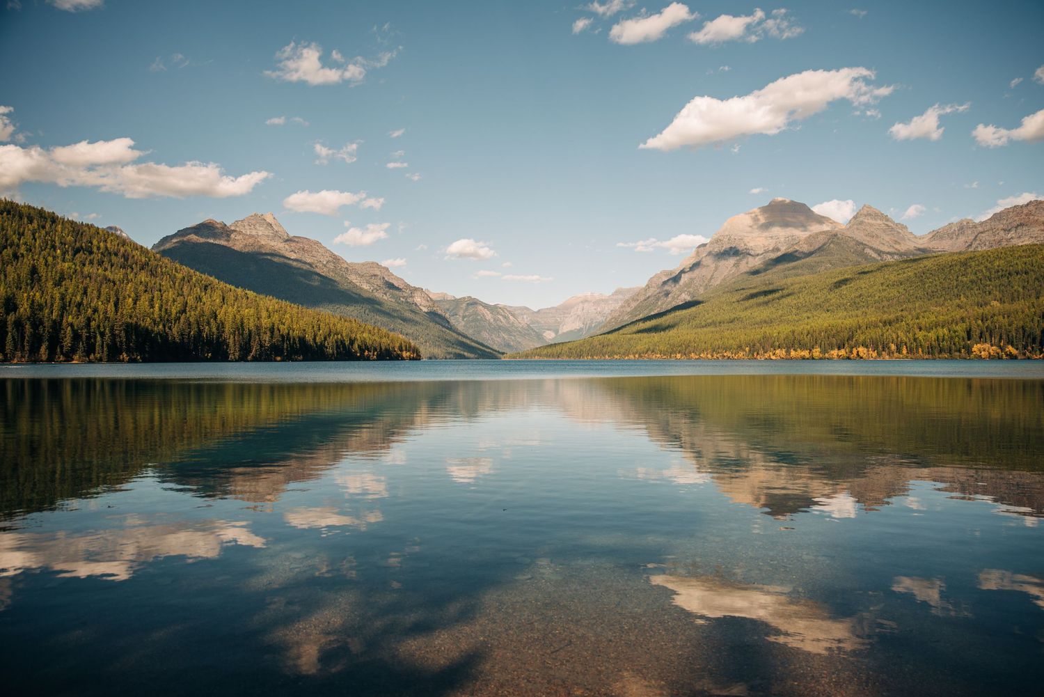 Tranquil mountain lake with perfect reflections of white clouds and forested peaks in calm waters during summer.