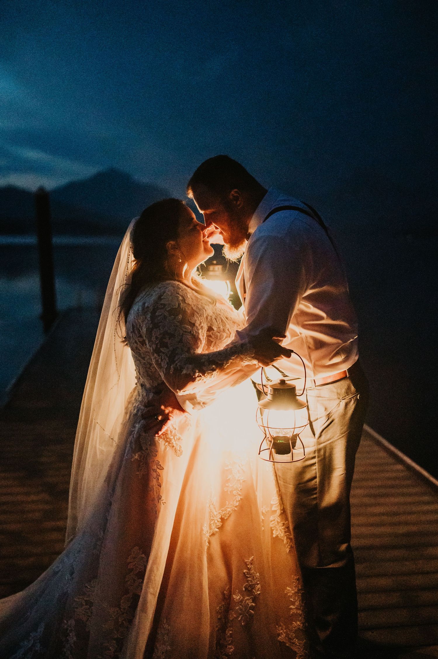 Romantic silhouette of a couple sharing an intimate moment on a dock with a lantern at dusk.