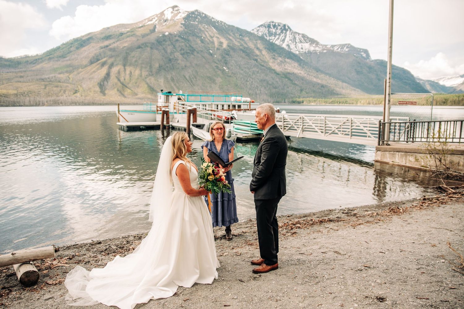 Two people having a romantic lakeside mountain wedding ceremony with scenic mountain peaks in the background.