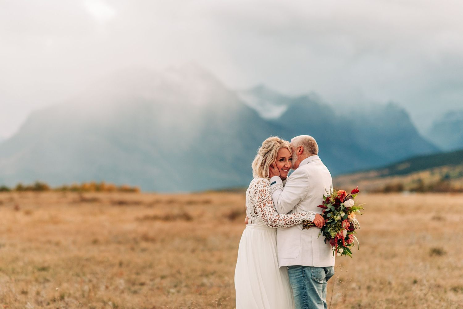 A romantic couple poses in a desert landscape against a backdrop of misty mountains during their elopement photo shoot.