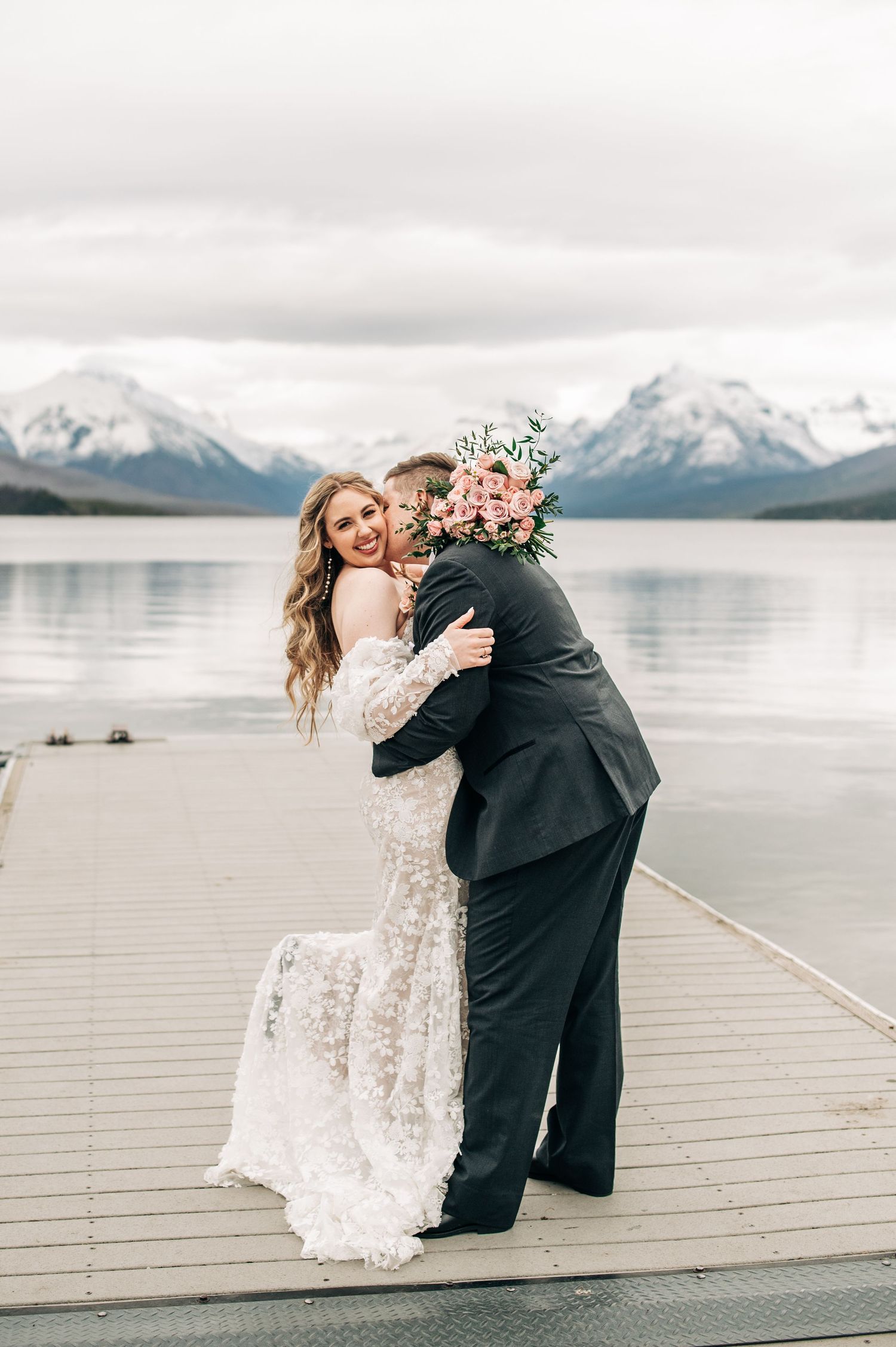 A romantic moment captured on a dock with snow-capped mountains and lake in the background.