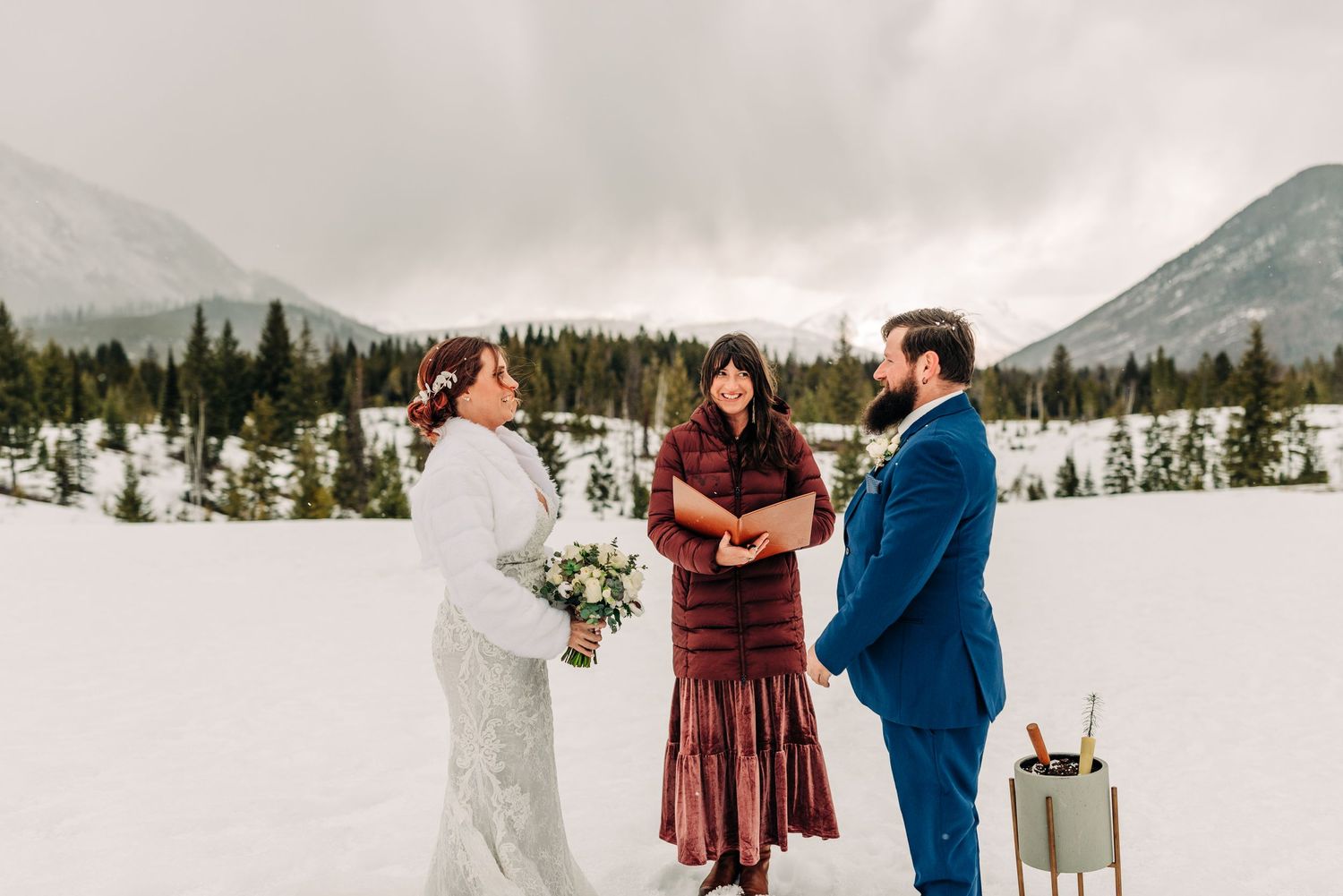 Intimate wedding ceremony in a snowy mountain landscape with evergreen forest backdrop.