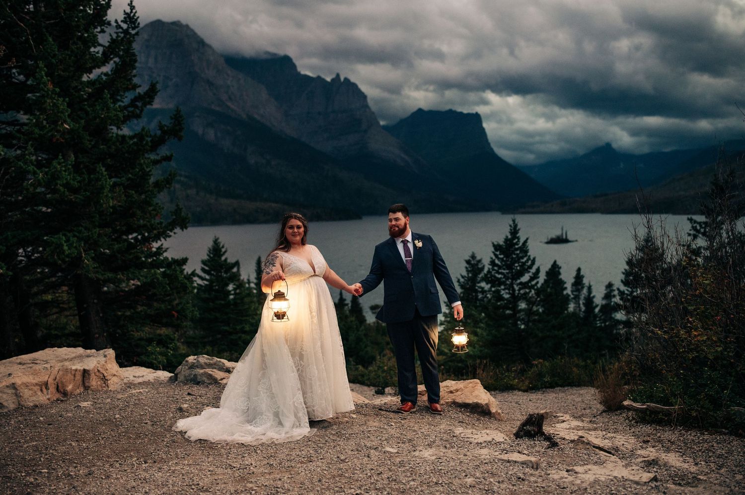 A couple stands on a mountain overlook with stormy skies above Banff Lake Minnewanka in the Canadian Rockies.