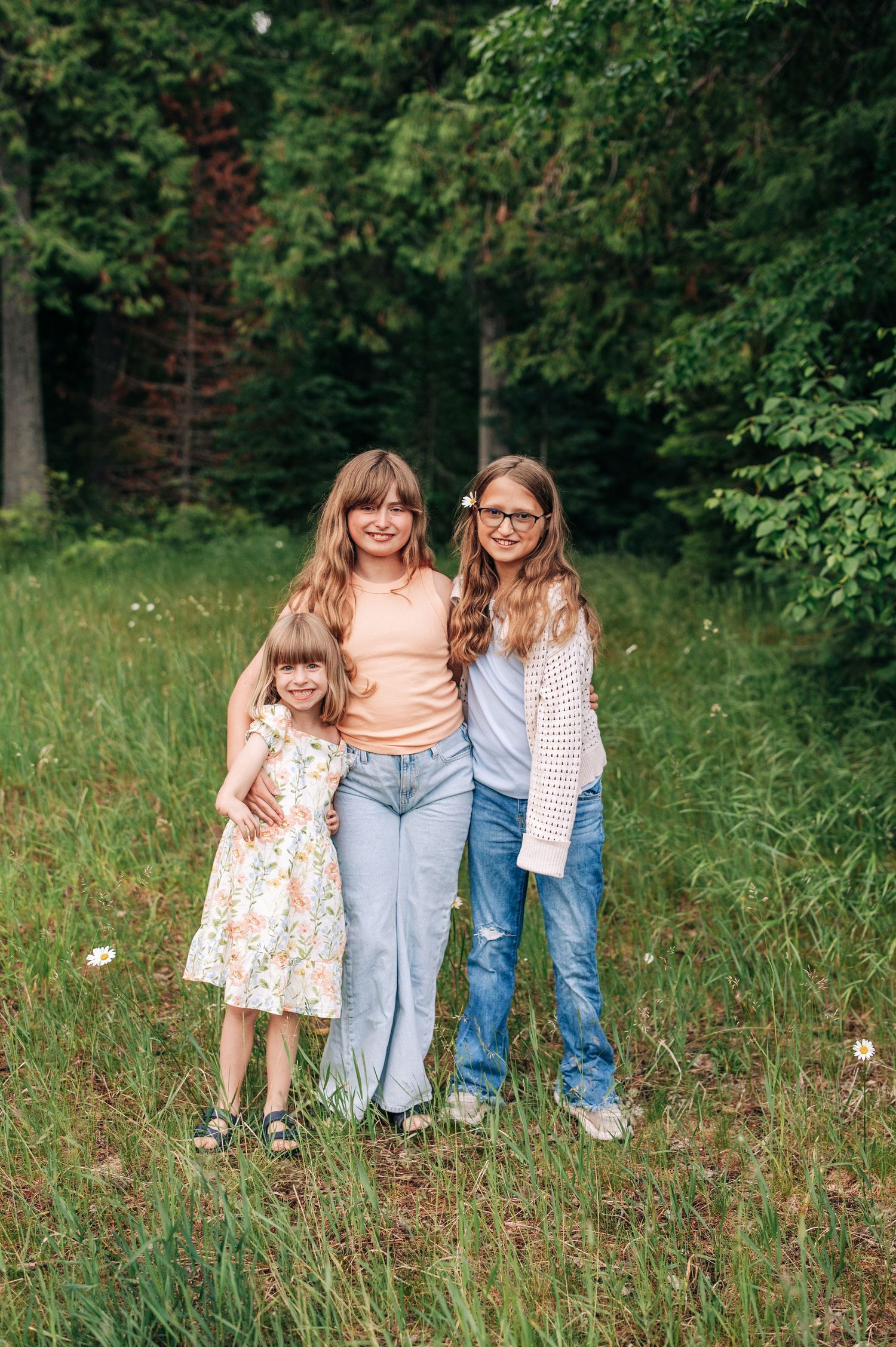 Three people stand together smiling in a grassy meadow with green forest trees in the background.