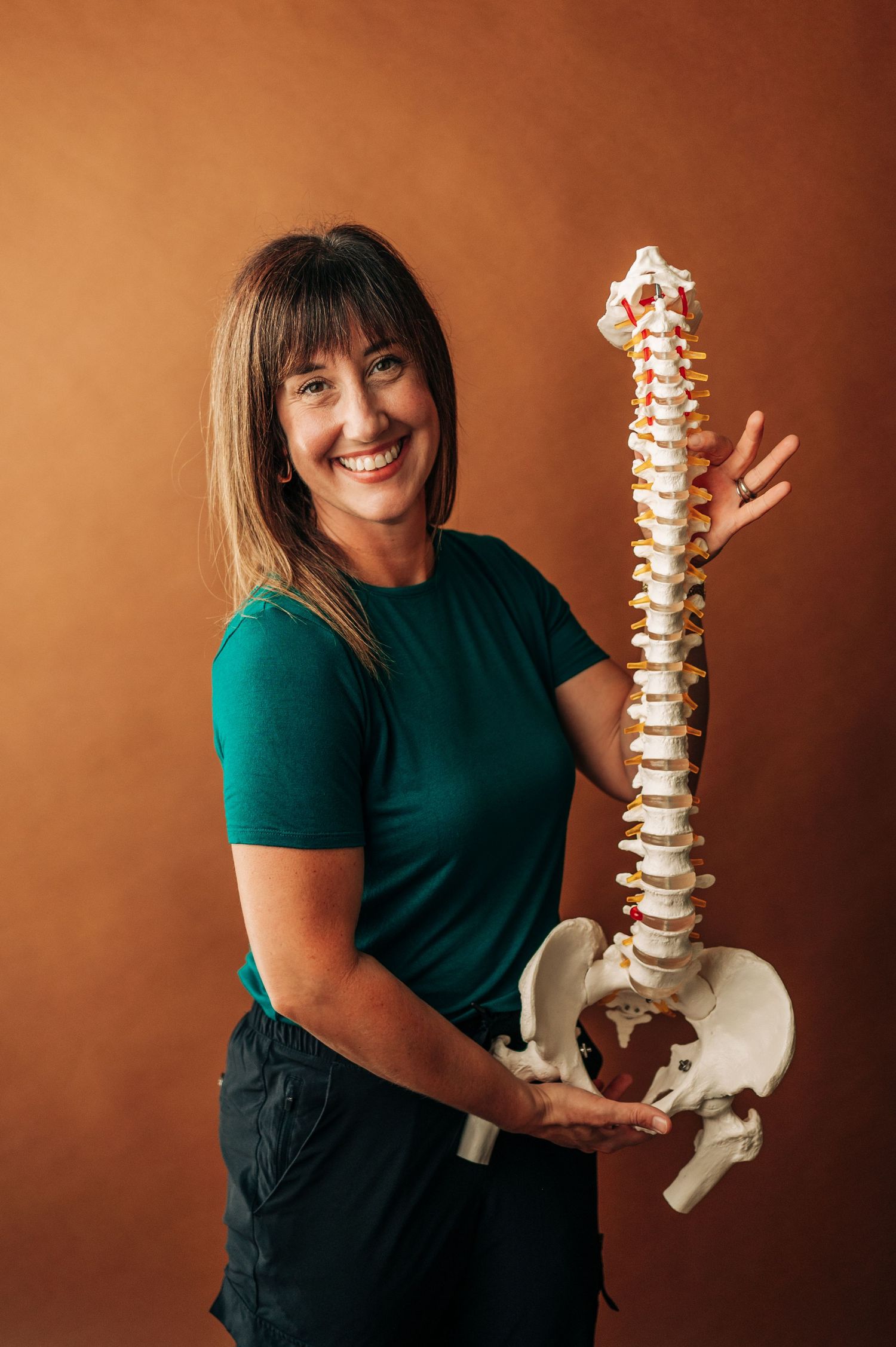 Healthcare professional in green shirt demonstrates spinal model against brown background in educational series.