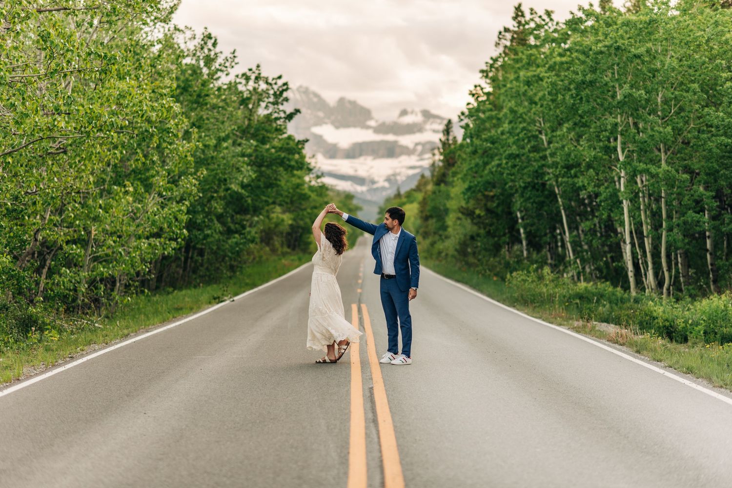 Two people in formal attire walking down a scenic tree-lined road on an overcast day.
