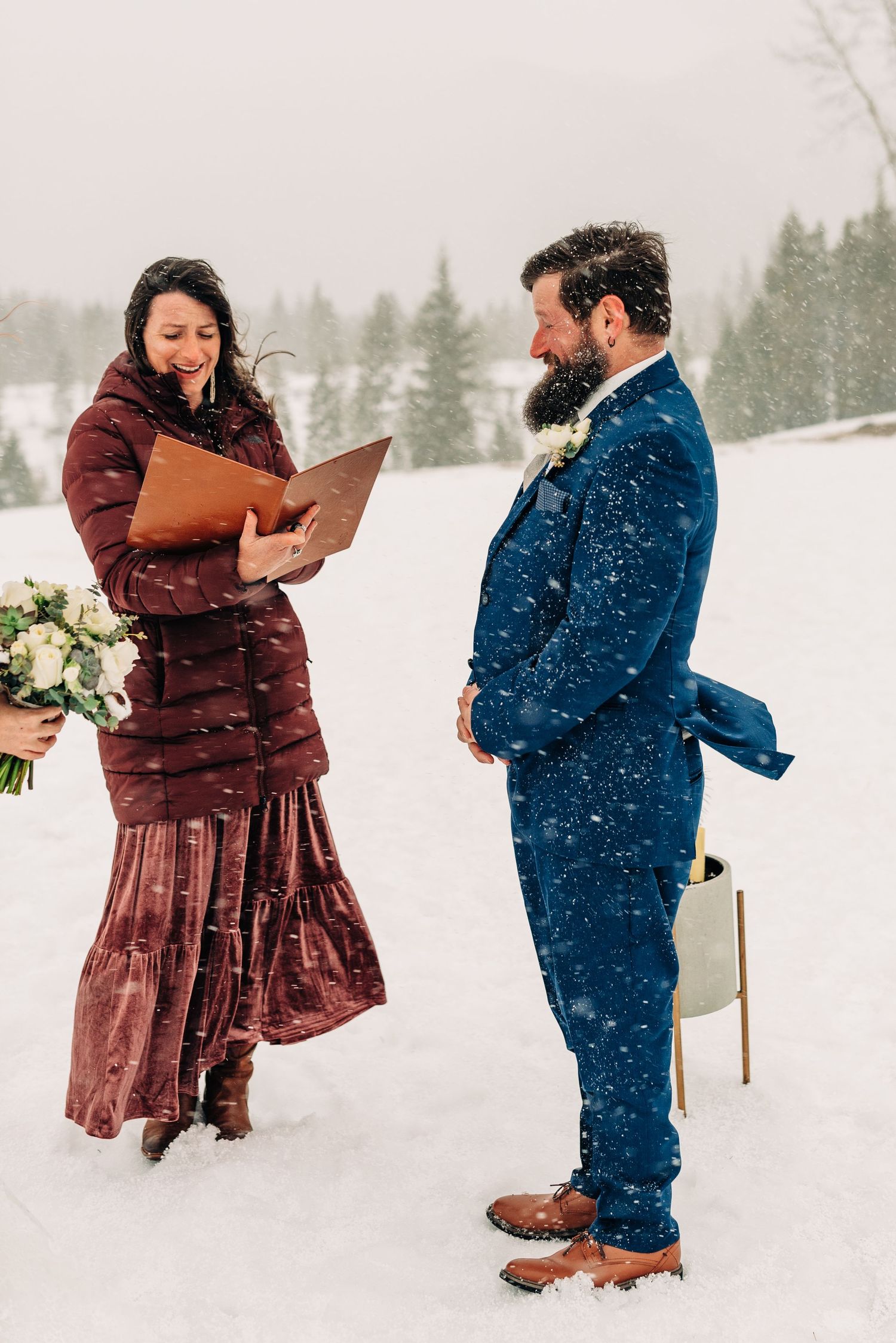 Winter wedding ceremony with snow falling in a mountain setting.