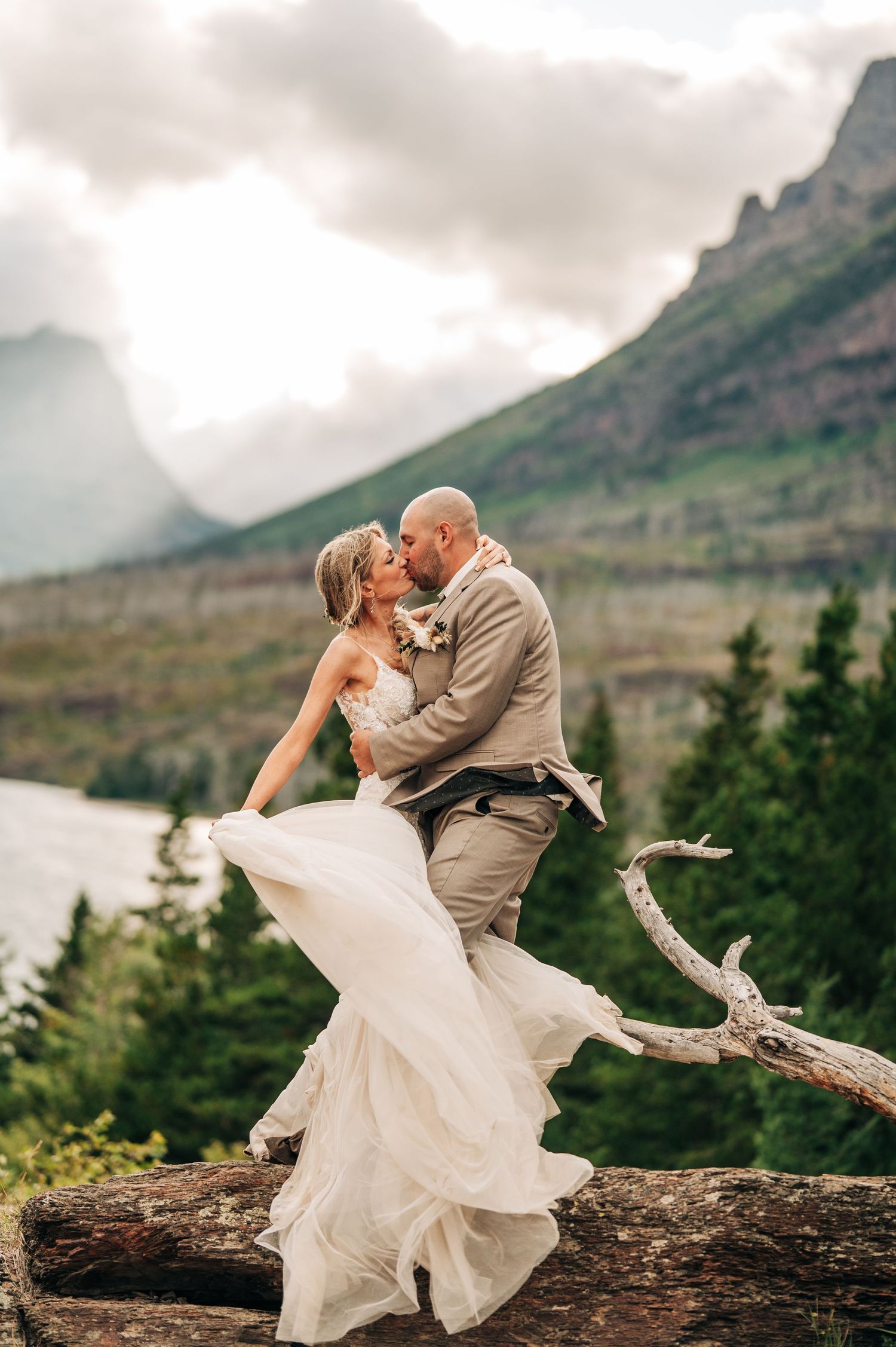 A romantic wedding portrait captured against the dramatic mountain landscape of Glacier National Park on a cloudy day.