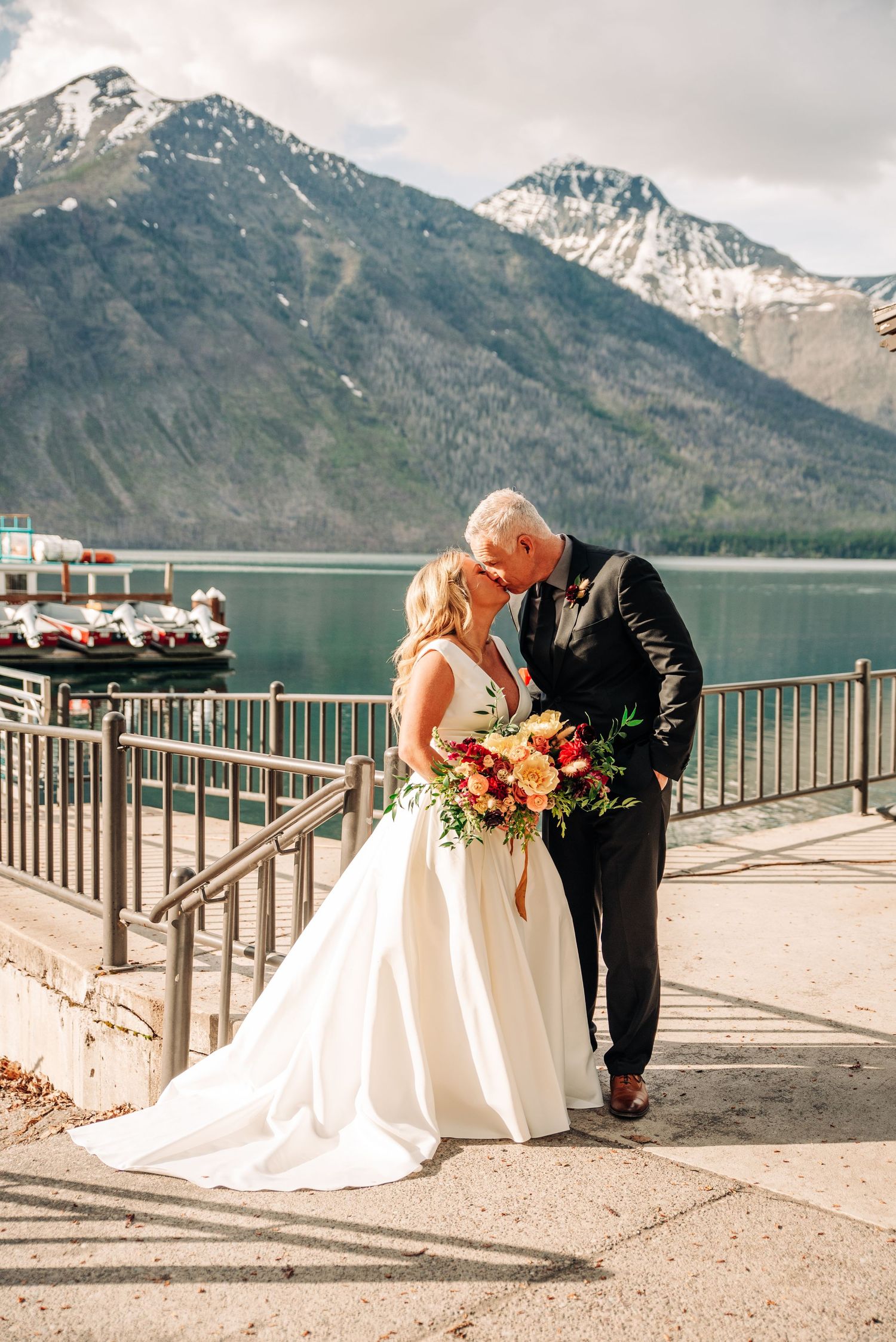 A couple shares a romantic moment by a turquoise lake with snow-capped mountains in the backdrop.