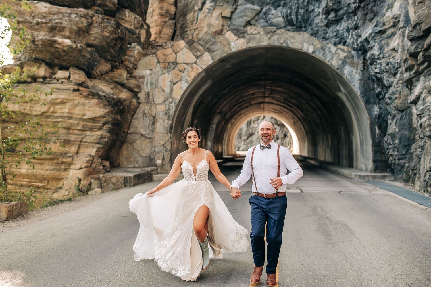 A newlywed couple strolls along a stone tunnel pathway in various poses during their outdoor photo session.