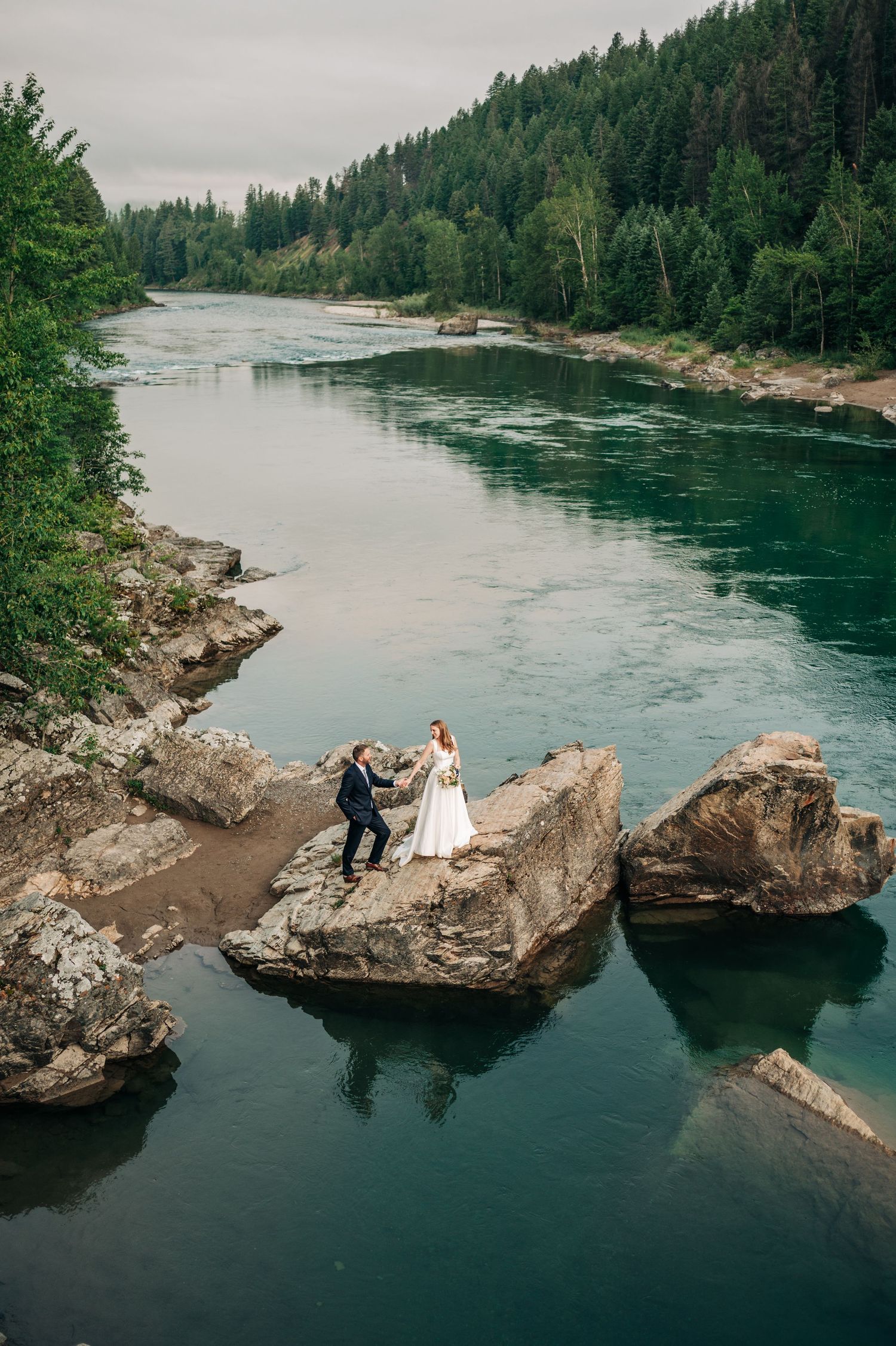 A series of aerial shots showing wedding portraits on dramatic rocky outcrops overlooking a scenic river with forest backdrop.