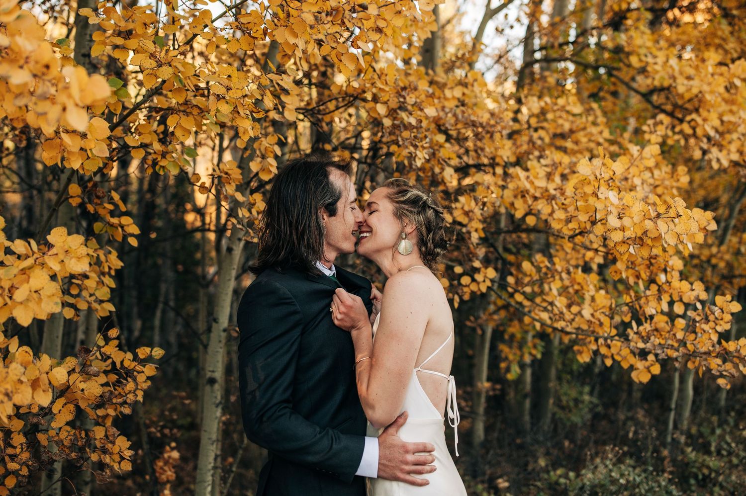 A romantic couple embraces in a forest surrounded by golden autumn foliage on a beautiful fall day.
