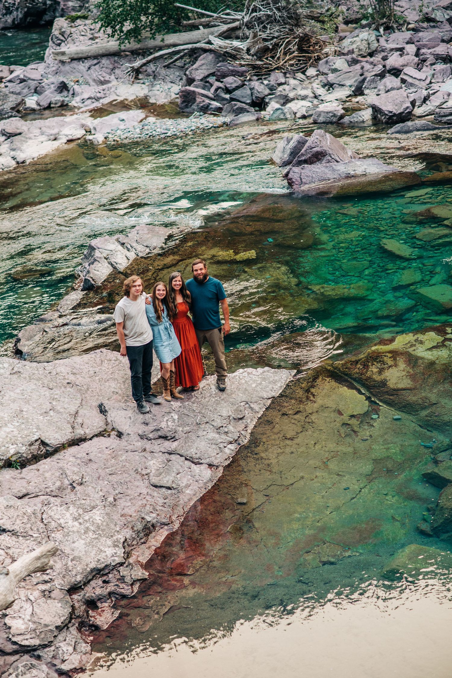 People standing on rocky cliff edge beside crystal clear turquoise mountain water in outdoor scenic landscape.