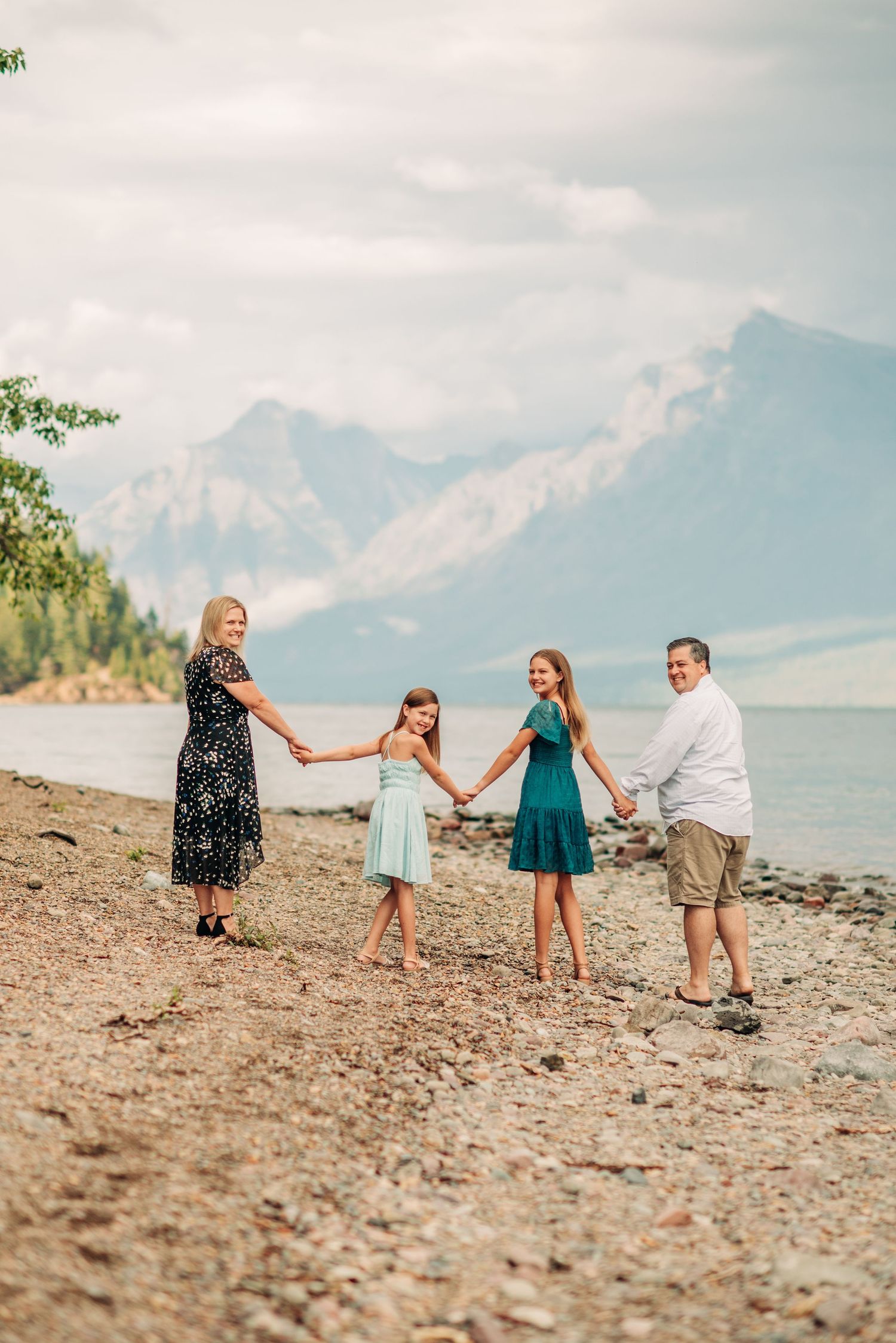 A family holds hands while standing on a rocky beach shore with misty mountains in the background.