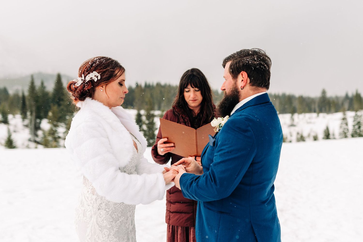 Wedding ceremony exchange of rings in snowy mountain setting.