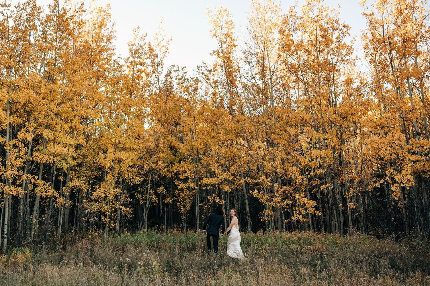 Two silhouettes stand together in front of golden autumn aspen trees in a scenic forest setting at sunset.