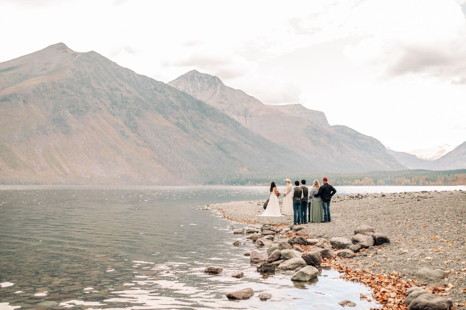 Three people stand on a rocky shore with mountains and a lake creating a scenic mountain landscape view.