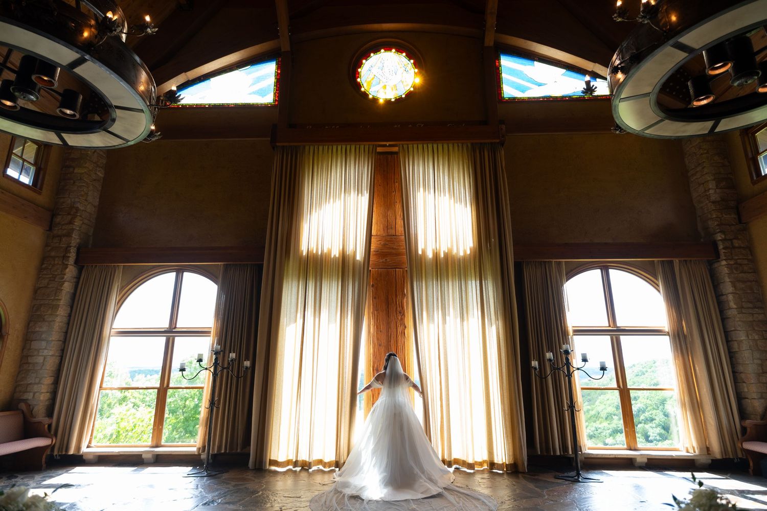Elegant bridal suite with arched windows, chandelier lighting, and sheer curtains creating a romantic atmosphere.