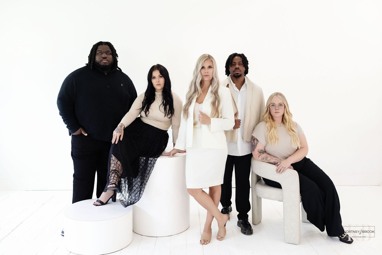 A diverse group of creative professionals posed together on white pedestals wearing coordinated black and white outfits.