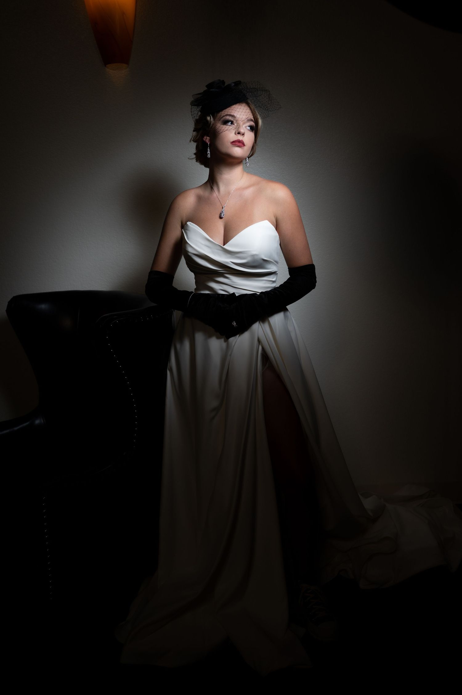 Elegant portrait of woman in white evening gown and black gloves in dramatic lighting.