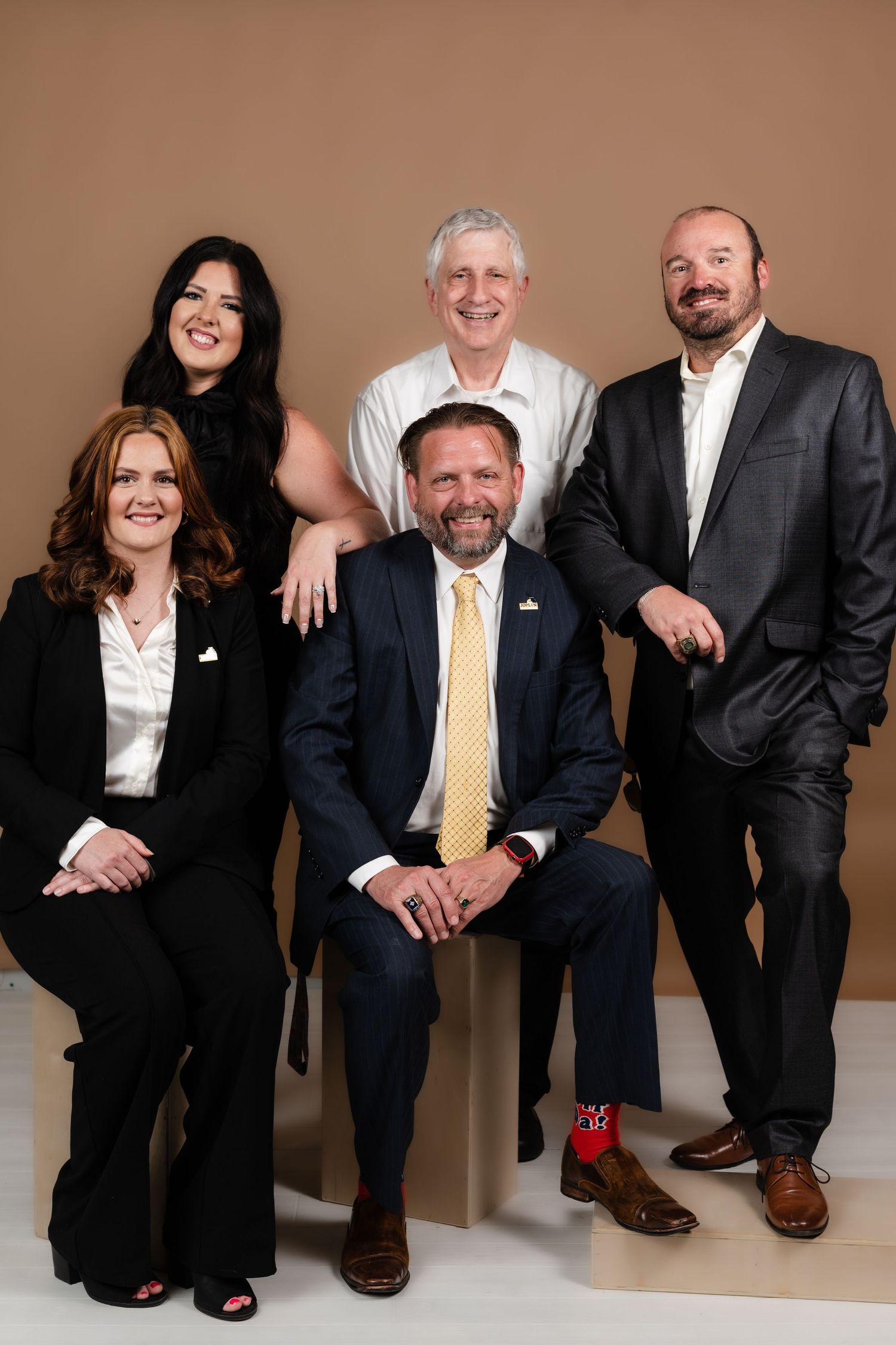 Professional group portrait in business attire against brown backdrop with warm lighting.