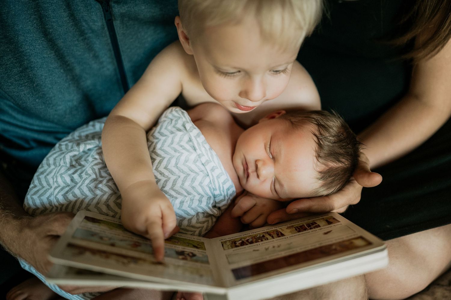 Children cuddled together reading story book on couch at home.