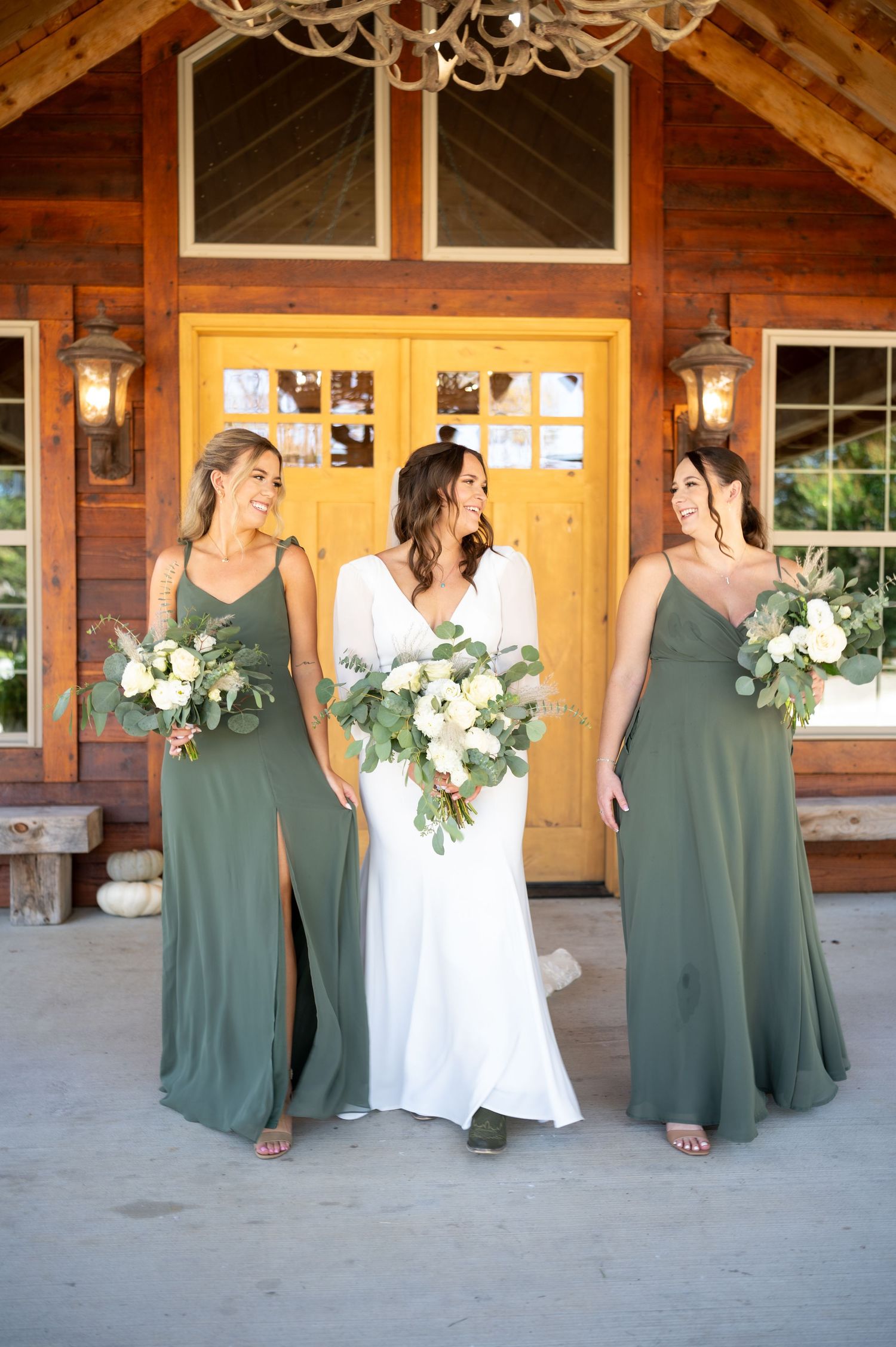 Wedding party in sage green dresses and white gown pose playfully in sequence outside rustic wooden venue.