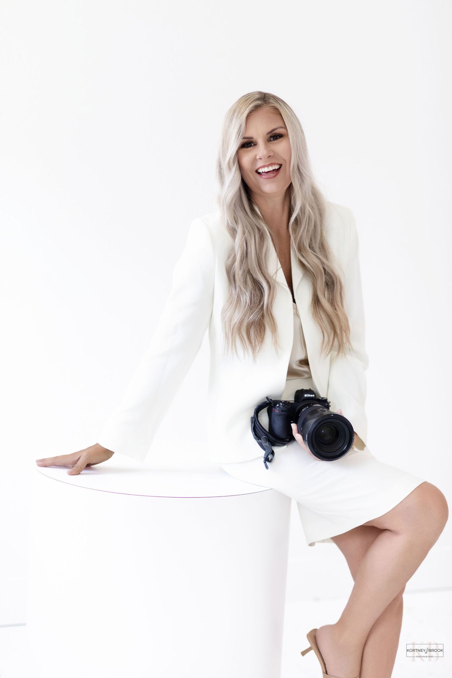 A studio fashion portrait featuring a white blazer and dress with professional camera.