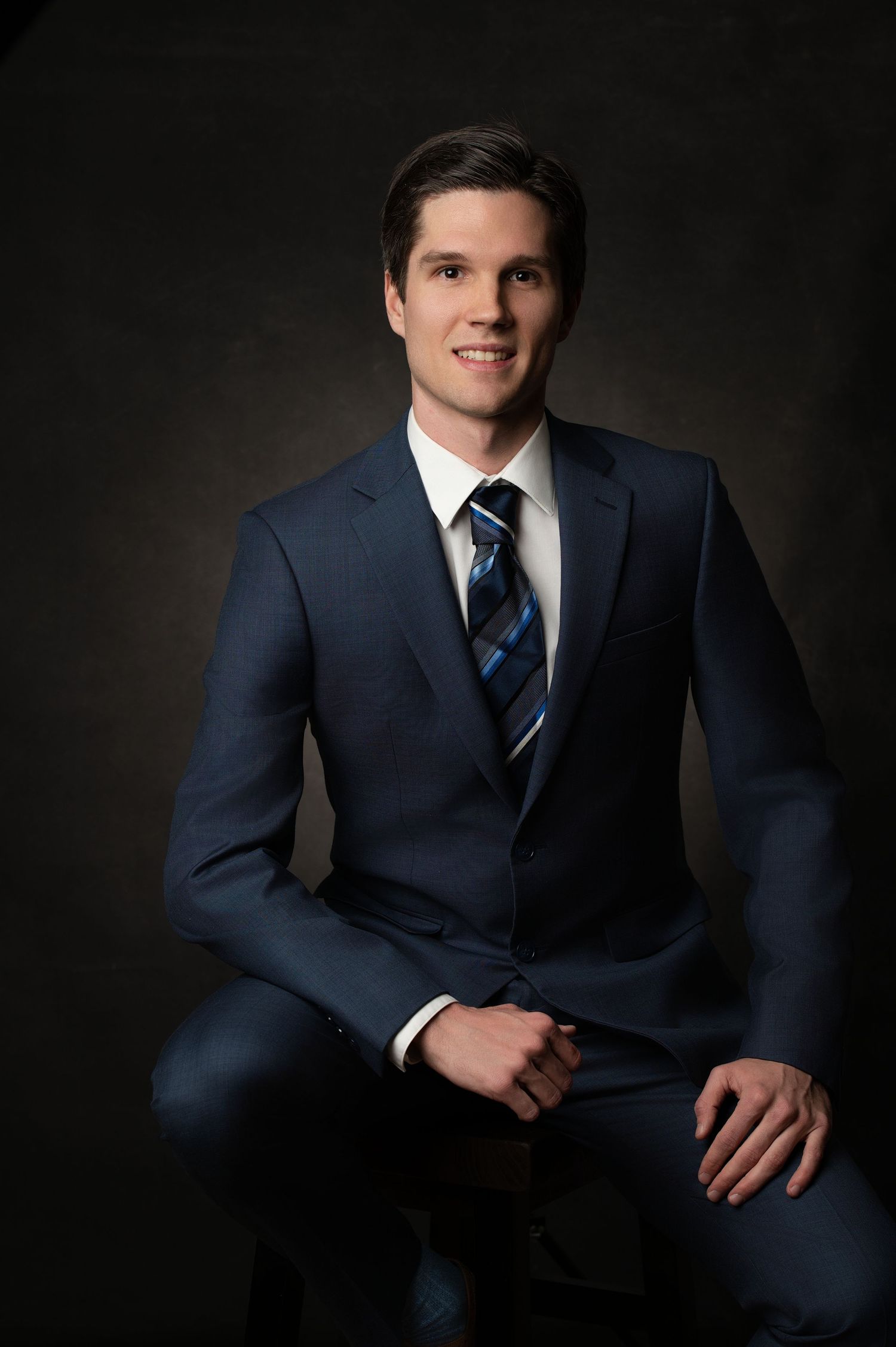 Professional studio portrait of a businessman in a navy suit against dark background.