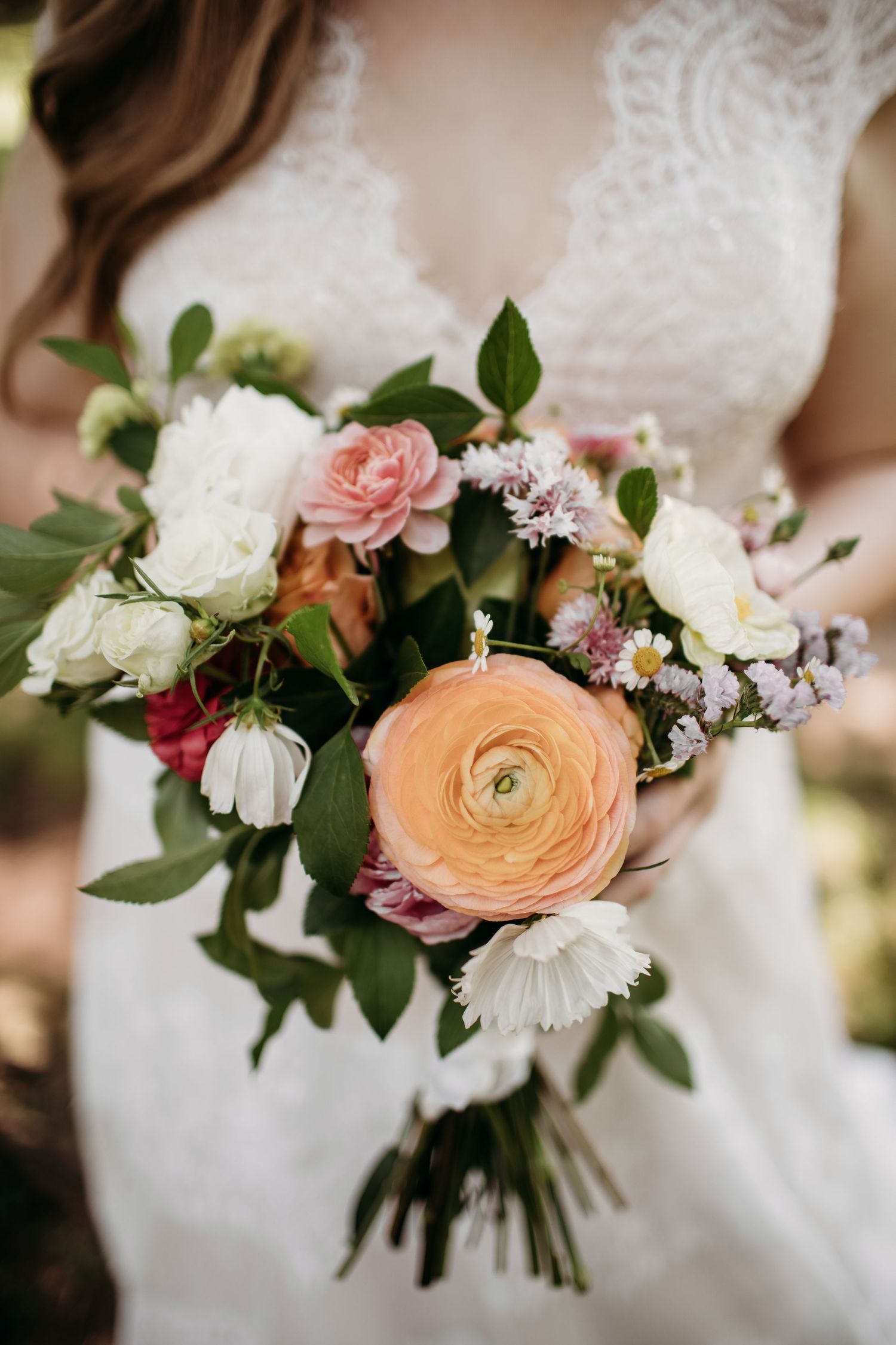 Beautiful bridal bouquet with peach ranunculus, pink roses, and white flowers with greenery.