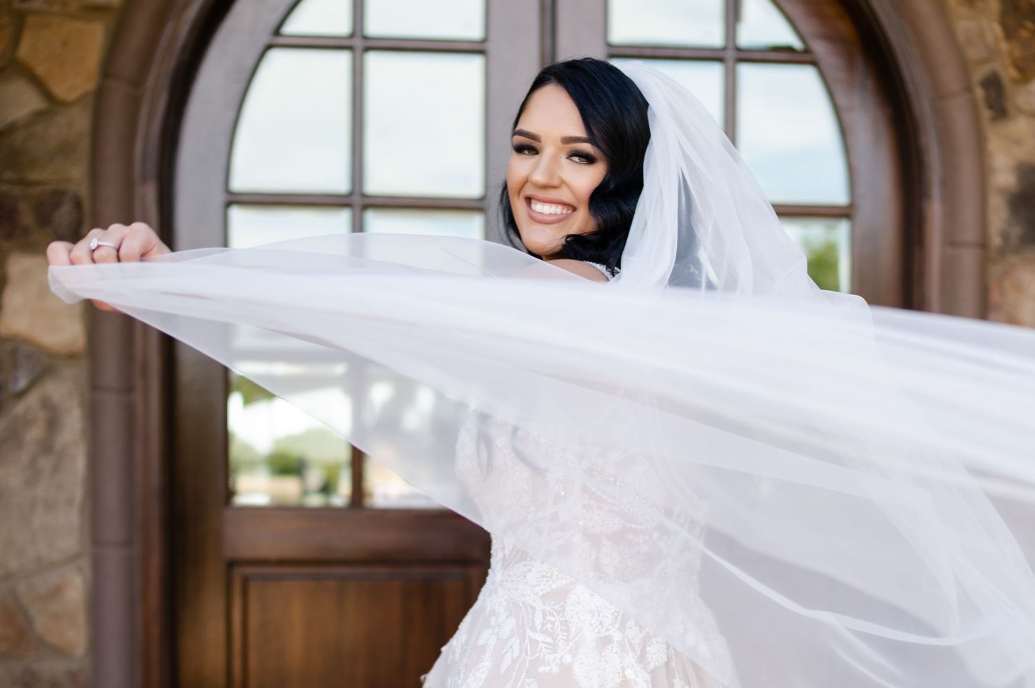 Flowing white veil creates dramatic movement in bridal portrait through arched doorway.