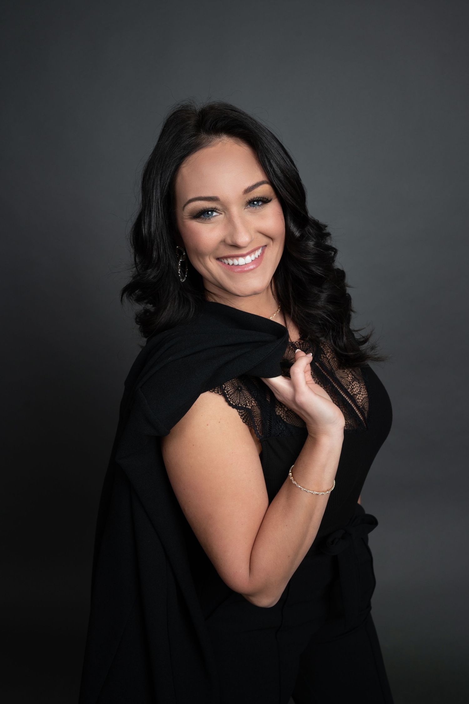 Studio portrait of woman in black dress with dark curly hair against gray background.