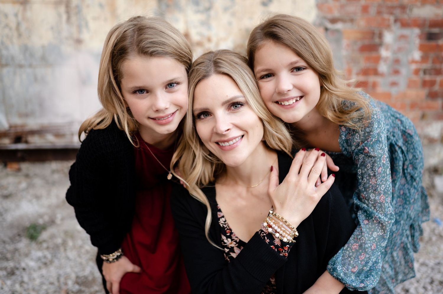 Three people pose together in an intimate family portrait against a brick wall.