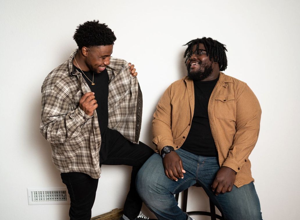 Two friends in casual attire having an animated conversation against a white background.