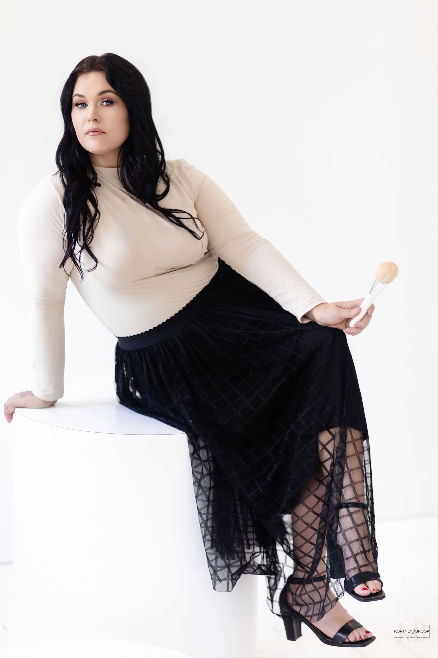 A fashionable studio portrait featuring a beige top and flowing black lace skirt against white background.