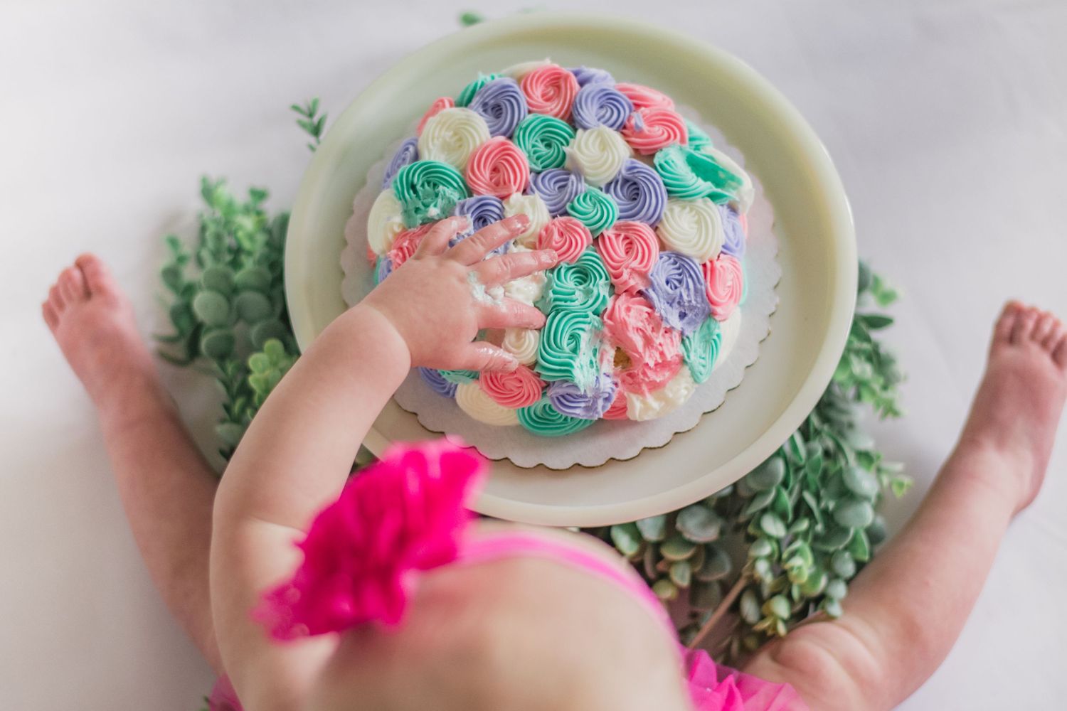 Small hands reach for a colorful birthday cake decorated with pink, blue and green frosting rosettes.