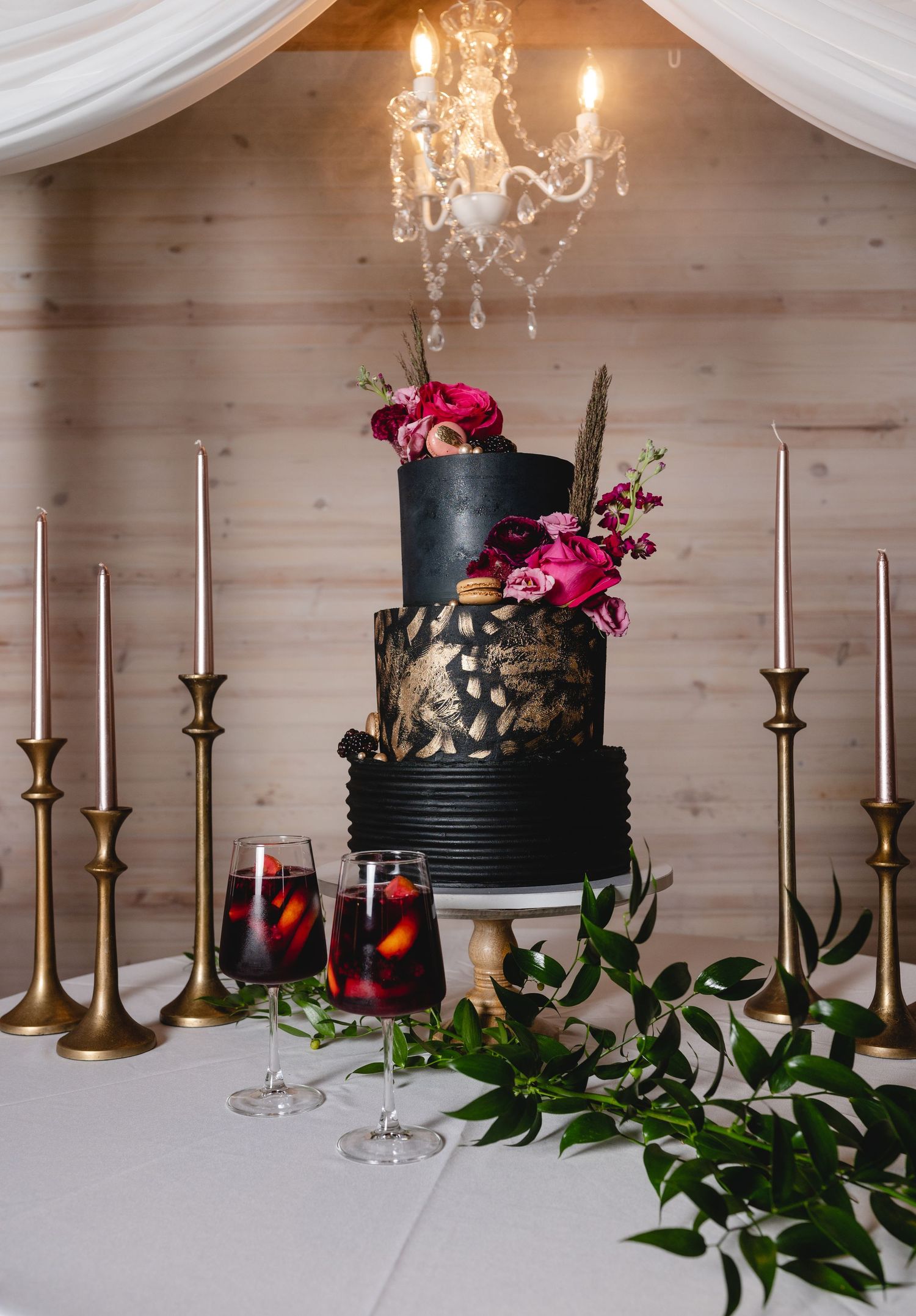 Elegant black and gold wedding cake with pink florals and taper candles in romantic setting.
