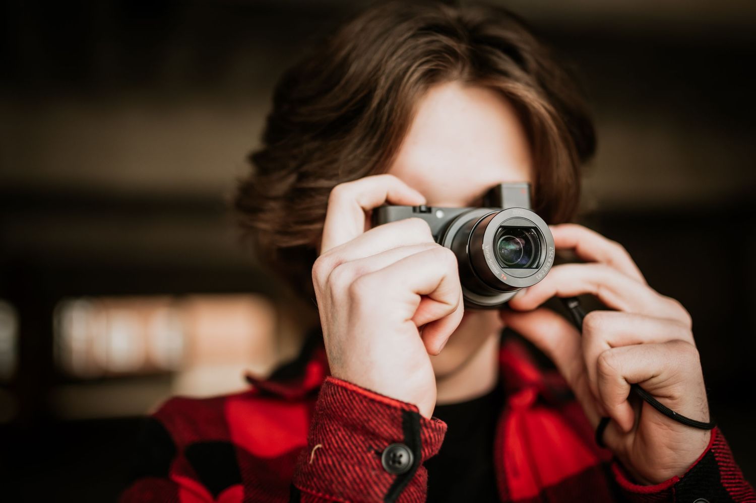 Close up shot of someone in red plaid shirt holding vintage camera to their eye.