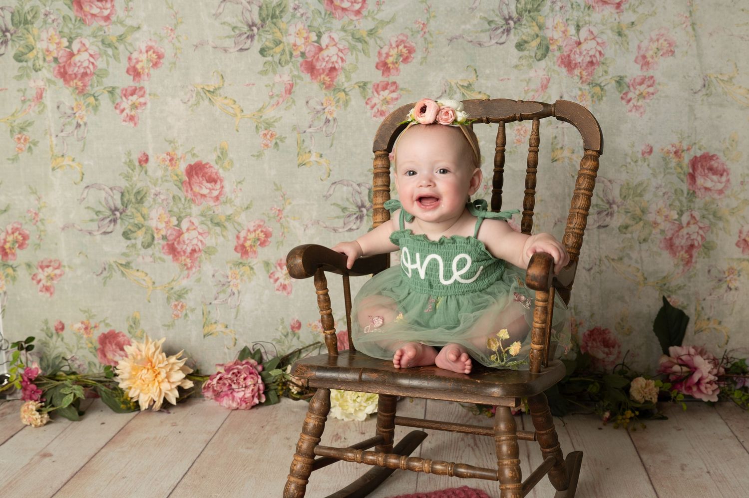 Vintage style baby photography setup with wooden chair and floral wallpaper background.
