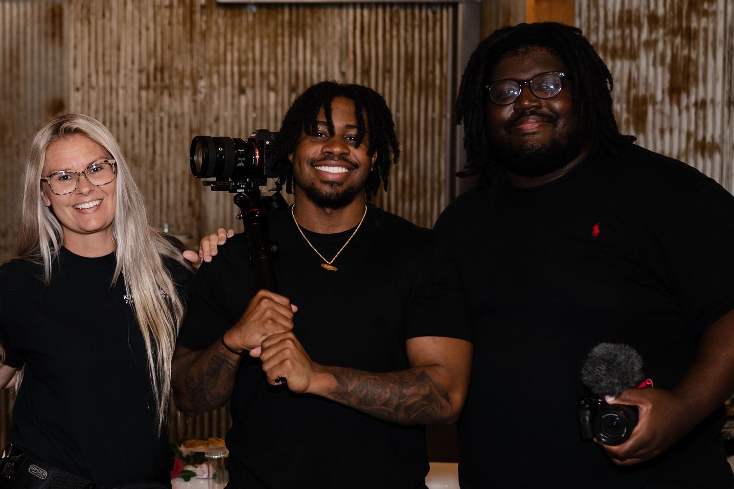 Photography team posing with cameras in a rustic indoor setting.
